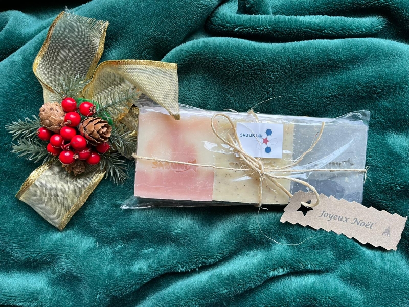 Photo de 3 savons parfumés, glissé dans un étui transparent à base d'amidon de maïs, sur fond vert.