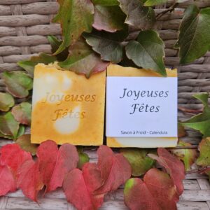 Savon estampillé et emballé avec le message « Joyeuses Fêtes » posé sur des feuilles de lierre.