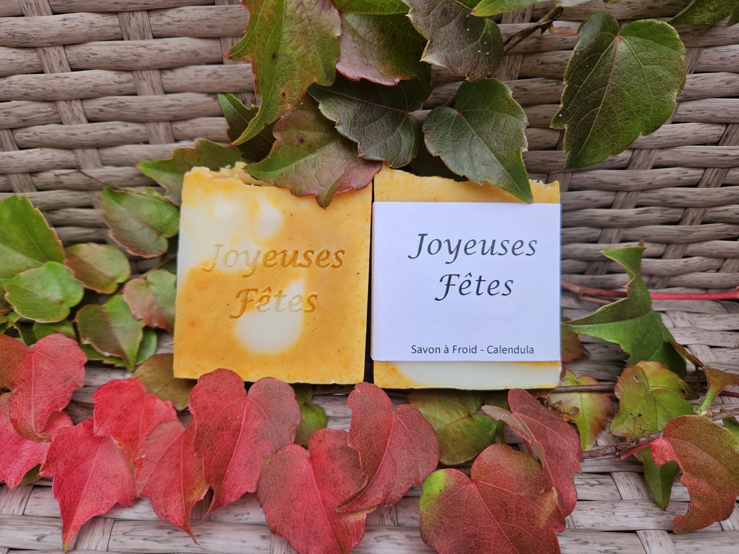 Savon estampillé et emballé avec le message « Joyeuses Fêtes » posé sur des feuilles de lierre.